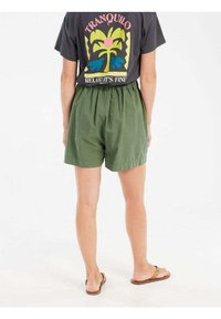 Groene, lichte shorts met een elastische taille, boven de knie lengte, gecombineerd met een zwart graphic t-shirt met een kleurrijk palmbomenontwerp.