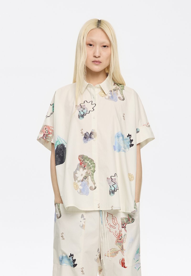 Camicia a maniche corte con bottoni in tessuto crema, caratterizzata da un mix di motivi astratti colorati ed elementi grafici.