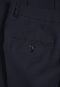 Tamsiai mėlyni pritaikyti kelnės su užsegama galine kišene ir subtilia tekstūra, plokščiu priekiniu paviršiumi ir diržo kilpomis.