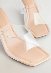Sandales à talons transparents avec une sangle transparente et un plateau nude. Présentent un orteil carré et un détail de couture le long des bords.