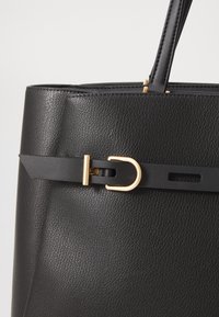 Black leather tote bag featuring a textured finish, gold-tone hardware, and a decorative strap with a loop detail.