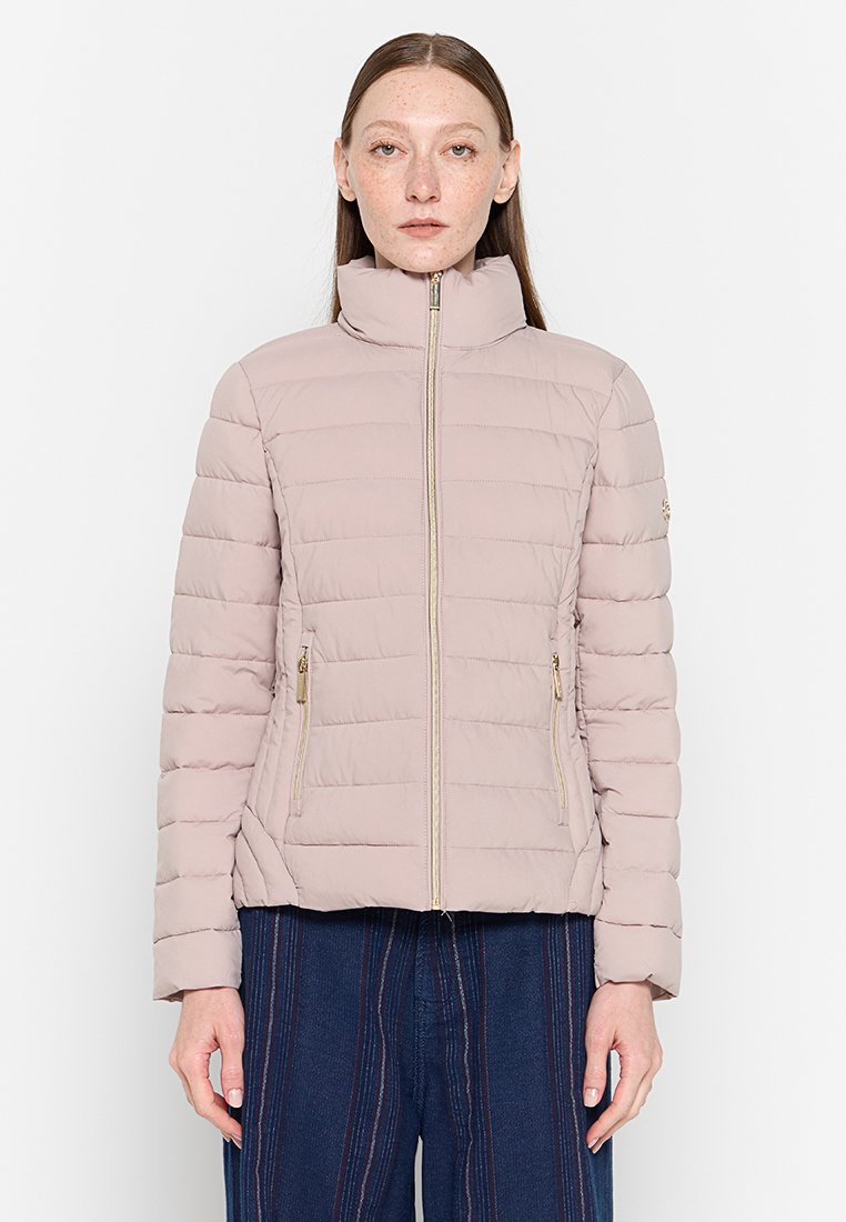 Giacca imbottita color beige chiaro con colletto alto, caratterizzata da una texture trapuntata verticale e tasche con zip dorate su ciascun lato.