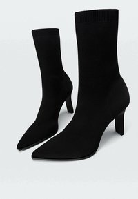 Bottes hautes à talons style chaussettes noires avec bouts pointus et dessus en tricot texturé. Dotées d'un talon bloc solide et d'une semelle lisse et plate.