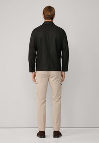 Zwarte jas met een gestructureerde kraag, gecombineerd met beige cargobroek met zijzakken, weergegeven vanuit de achterkant. Vlak, textuurstof.