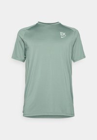 Πράσινη αθλητική μπλούζα φτιαγμένη από απαλό, ελαφρύ υλικό. Διαθέτει κοντό μανίκι, στρογγυλή λαιμόκοψη και διακριτικά λογότυπα στη θηλή.