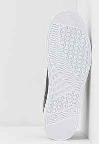 Semelle d'une basket avec une semelle en caoutchouc blanc présentant des motifs hexagonaux, en zigzag et en grille, marquage de taille "37" visible près du centre.