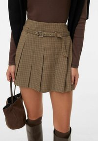 Bruine geruite rok met plooien, riemdetail en zijzakken. Gecombineerd met een bruine tas en kniehoge laarzen.