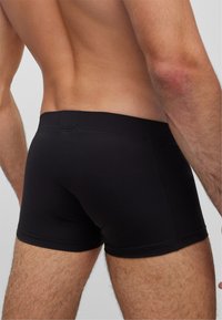 Boxers negros elásticos con un diseño ajustado, textura suave y detalles cosidos alrededor de la cinturilla y las aberturas de las piernas.