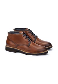 Botas de tobillo de cuero marrón con textura suave, punteras redondas y cordones oscuros. Cuentan con una suela de goma con un detalle de costura en contraste.