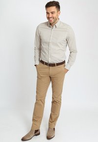 Lichtkleurig overhemd met kleine donkere stippen, gecombineerd met beige chinos en bruine Chelsea boots. Soepele stof en op maat gemaakte pasvorm.