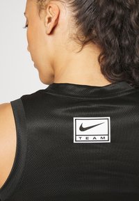 Černý sportovní top bez rukávů s texturovaným povrchem, na zadní straně s čtvercovým logem Nike a slovem "TEAM" pod ním.