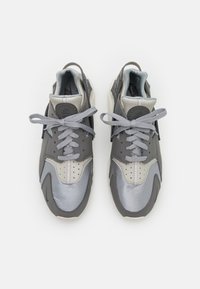 Šedé tenisky mají kombinaci kožených a textilních materiál ů, s hladkým povrchem, kulatou špičkou a kontrastními akcenty v světlejší šedé barvě.