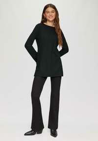 Schwarzes, geripptes Langarmoberteil mit Rundhalsausschnitt, kombiniert mit schwarzen, weit geschnittenen Hosen und spitzen, hohen Stiefeln. Glatte Textur über das gesamte Kleidungsstück.