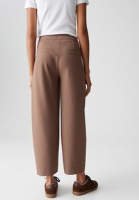 Bruine brede broek met achterzakken, een gladde textuur en een op maat gemaakte uitstraling, gecombineerd met donkere sneakers en een wit shirt.