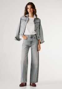 Chaqueta de mezclilla azul claro sobre una camiseta blanca, combinada con jeans de pierna ancha azul claro y zapatillas burdeos.