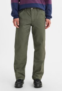 Olivgröna byxor med rak ben design, tillverkade av slitstarkt bomullsmaterial. Har framfickor och knappstängning.