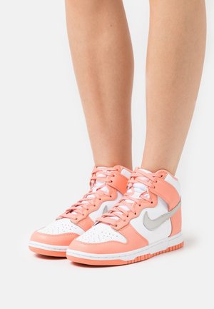 Hoge sportsneakers met wit leer, perzikkleurige suède accenten, geperforeerde neus en een zilveren Nike Swoosh-logo.
