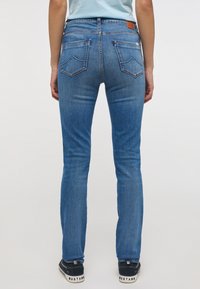 Kék farmernadrág, slim fit szabással, világos mosással, finom koptatással és hímzett hátsó zsebekkel, sötét tornacipővel párosítva.