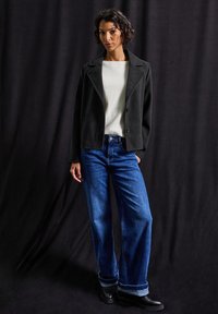 Black tailored blazer over a white top, paired with loose blue denim jeans and black ankle boots. Textured materials evident in fabrics.
