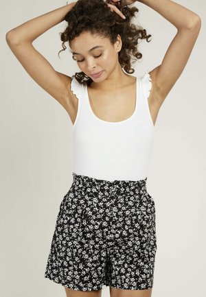 Débardeur blanc à côtes avec des bretelles volantées, associé à un short noir taille haute présentant un petit motif floral blanc.