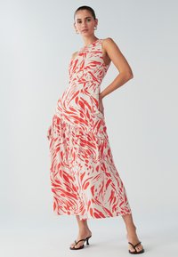 Maxikleit punase ja valge keerleva mustriga, millel on ühe õla disain, talje sisse tõmmatud ja astmelise seelikuga. Sile kanga tekstuur.