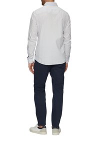 Witte shirt met kleine blauwe geometrische patronen, lange mouwen, met knoopsluiting op de kraag, gecombineerd met donkere broek en casual witte sneakers.