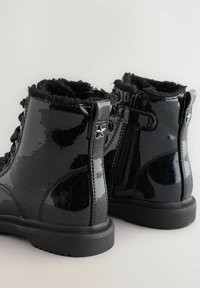 Schwarze Lackleder-Stiefeletten mit einem strukturierten schwarzen Fellfutter, Glitzermotiven und einem seitlichen Reißverschluss mit einem sternförmigen Detail.