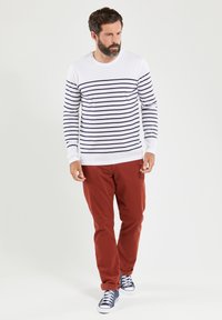 Langærmet hvid skjorte med marineblå horisontale striber, parret med røde bukser og blå sneakers. Har en rund halsudskæring og tætsiddende design.
