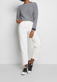 Haut à manches longues rayé avec des accents bleu marine, associé à un jean droit blanc et des baskets montantes noires avec semelles et œillets blancs.