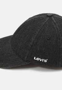 Gorra de béisbol de denim negro con visera curvada, logo blanco de "Levi's", superficie texturizada y detalles de costura en contraste.