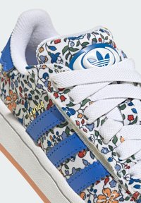 Floral print sneaker features a white fabric upper with multicolored flowers, blue leather stripes, white laces, and a textured rubber sole.