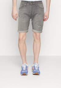 Pantalones cortos de mezclilla gris con un diseño desgastado, con dobladillos enrollados, bolsillos delanteros y traseros, combinados con zapatillas deportivas azules.