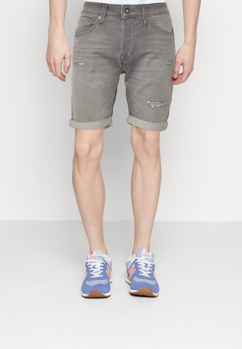 Pantalones cortos de mezclilla gris con un diseño desgastado, con dobladillos enrollados, bolsillos delanteros y traseros, combinados con zapatillas deportivas azules.