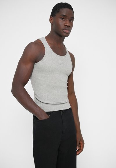 Sivý tielkový top s priliehavým strihom a rebrovanou textúrou. Má okrúhly výstrih a malé logo vpredu. Kombinovaný s čiernymi nohavicami.