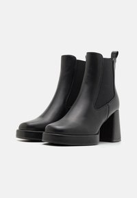 Bottines en cuir noir avec des panneaux latéraux élastiques, des orteils arrondis et des talons carrés. Texture lisse et design minimaliste.