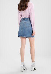 Ljusblå denim A-linje kjol med bakfickor och en fransad nederkant. Matchad med silvriga ankelskor och en rosa tröja med en rosett. 