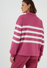 Felpa rosa con strisce orizzontali bianche, design con colletto, vestibilità comoda e polsini a coste. Abbinata a pantaloni rosa coordinati.