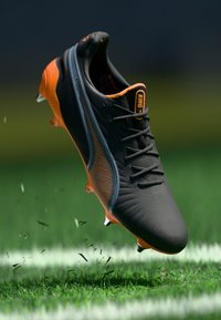 Scarpa da calcio nera e arancione con un design elegante, tomaia testurizzata e forma angolare, caratterizzata da un motivo a strisce unico e tacchetti.