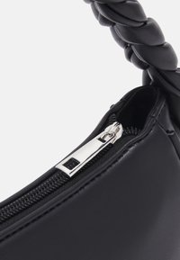 Melnā sintētiskā soma ar pītas rokturi un sudraba zipsa detaļām. Gluda tekstūra ar kontrastējošu auduma iekšpusi.