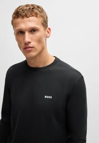 Tricou negru cu mânecă lungă, realizat dintr-un material neted, cu guler rotund și logo-ul alb "BOSS" pe pieptul stâng.