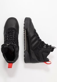 Bottes de randonnée noires combinant cuir et suède. Tige texturée, col rembourré et languette de tirage rouge contrastante avec une semelle robuste.