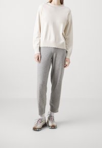 Sweter w kremowym beżu, z okrągłym dekoltem i prążkowanymi mankietami. Połączony z jasnoszarymi, luźnymi spodniami dresowymi i sportowymi trampkami z akcentami.