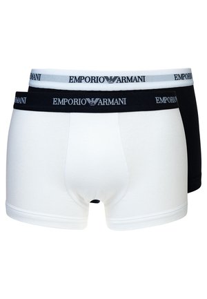 Deux paires de trunks en coton : une blanche avec une taille et un logo noirs, l'autre noire avec une taille et un logo blancs. Les deux sont extensibles et ajustés.
