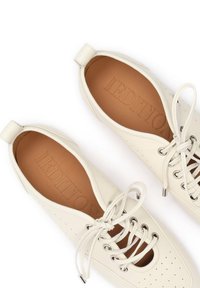 Chaussures blanches en cuir à lacets avec détails perforés et semelles intérieures marron embossées du nom de la marque, vues de dessus sur fond blanc.
