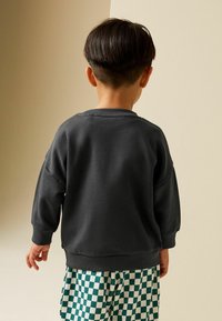 Tmavě šedá mikina s dlouhými rukávy, žebrovanými manžetami a kulatým výstřihem, kombinovaná s kalhotami se vzorem zelenobílých kostek.