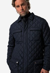 Granatowa pikowana kurtka z diamentowym wzorem, dwiema kieszeniami na piersi i zatrzaskowymi akcentami. Wykonana z ocieplanej, wodoodpornej tkaniny.
