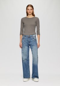 Graues langärmliges Oberteil und hellblaue weite Jeans. Die Jeans haben einen verblassten Look und Vordertaschen; das Oberteil hat einen runden Halsausschnitt. Weiße Sneakers.