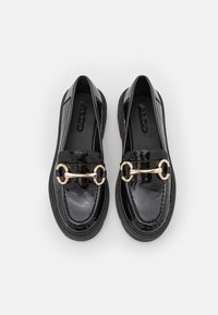 Pár černých lakovaných polobotek s detailem zlatého koňského bitu, silnými podrážkami a značkou embosovanou na vnitřní podrážce.