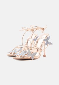 Sandały na wysokim obcasie w kolorze różowego złota z cienkimi paskami, ozdobione niebieskimi kryształkami w kształcie motyla na palcach oraz z otwartym tyłem.