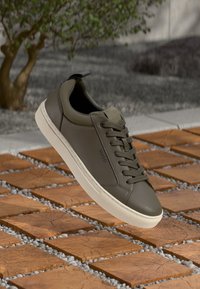 Olivengrønne lædersneakers med en glat overflade, snørebånd foran og hvid gummisål. Har "HUGO" branding på siden.